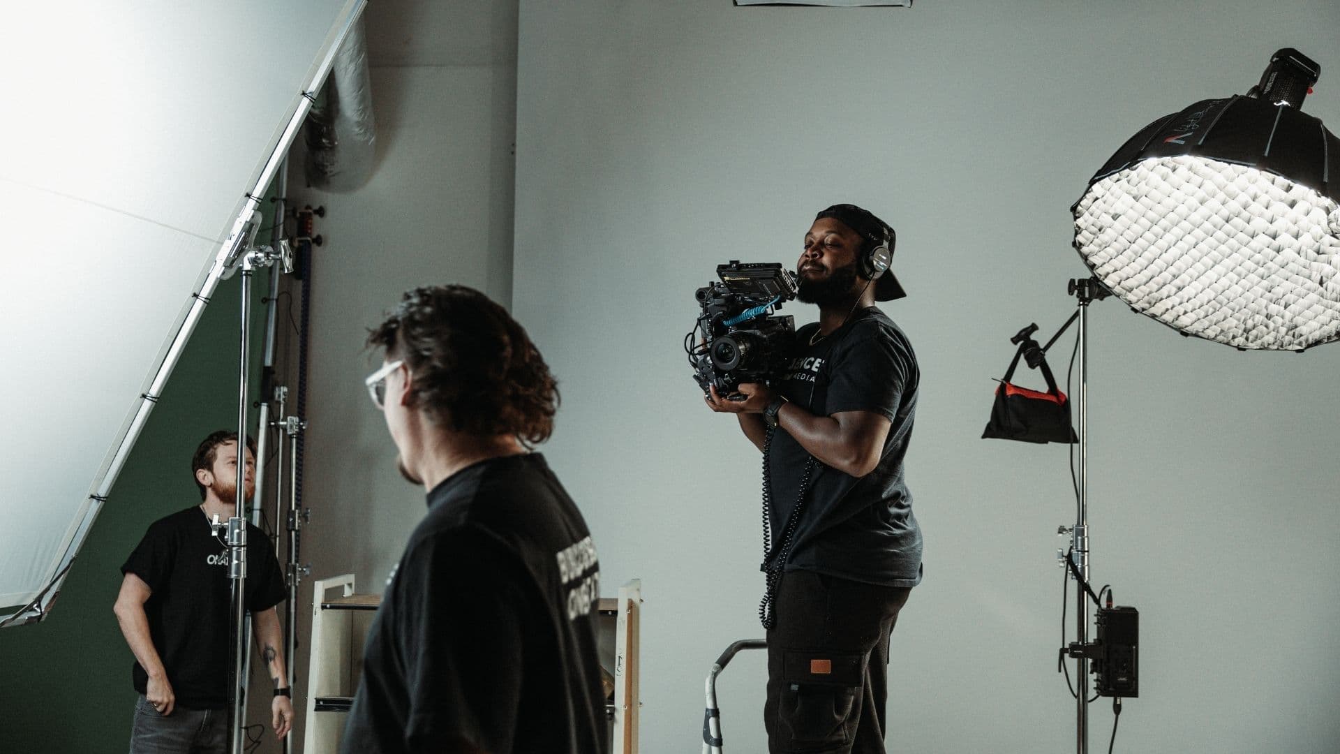 Camera operator filming talent against a gray seamless cyclorama with a softbox overhead