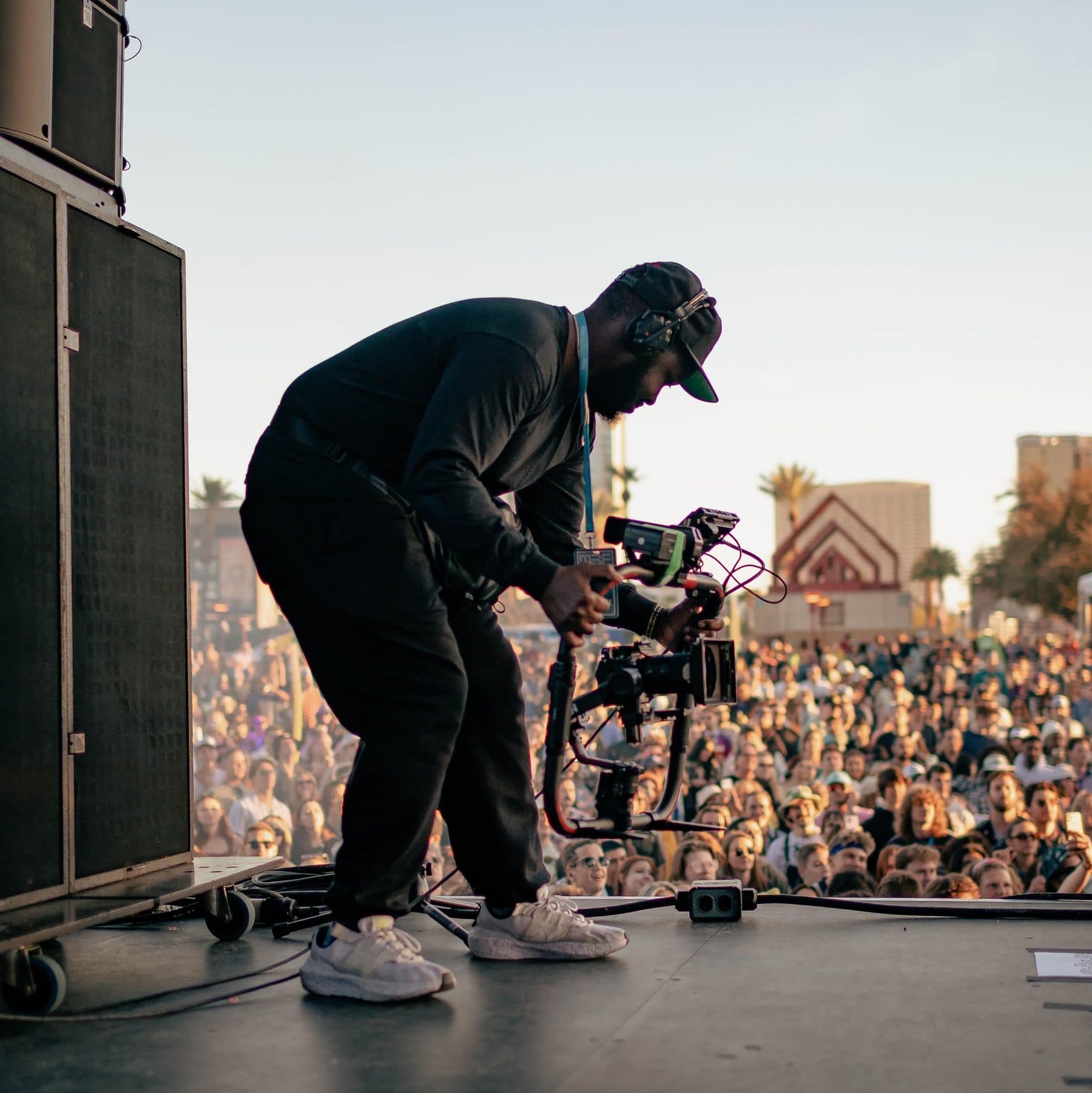 Camera operator on a festival stage filming the crowd with a gimbal rig at sunset