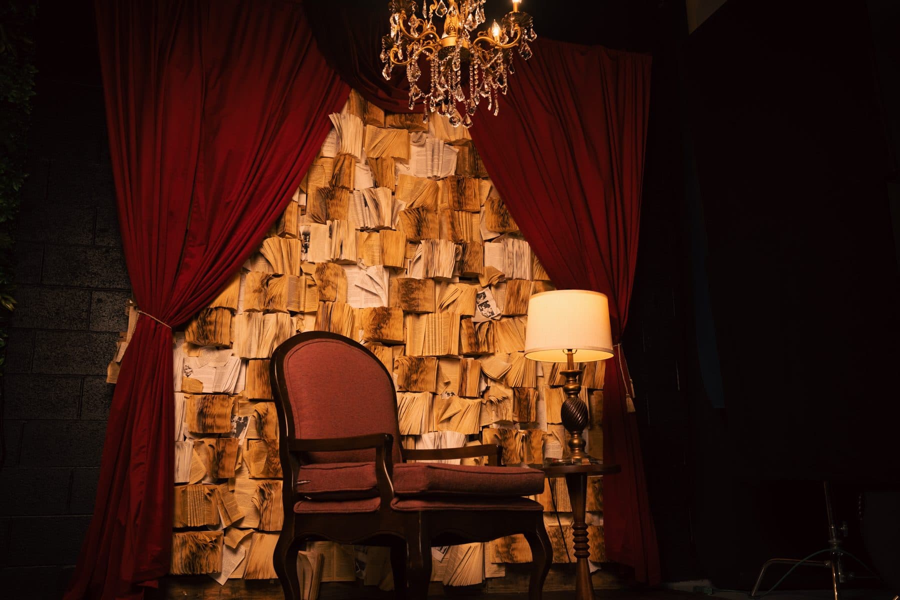 Book wall set at Influence Studios with red curtains, a chandelier and an armchair
